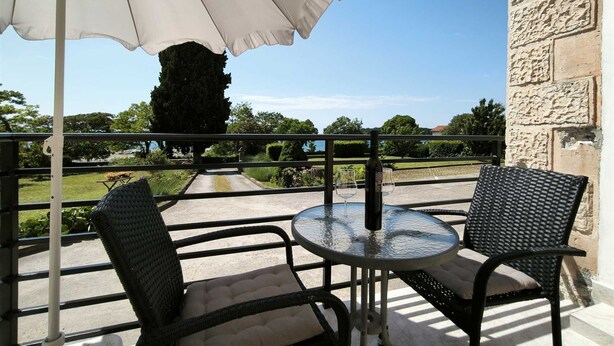A balcony with two wicker chairs, a round glass table, and a large white umbrella. - MATIKA One-Bedroom Apartment with Terrace (Rovinj)