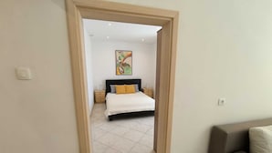 A bedroom with a bed, a nightstand, a painting on the wall, and a door leading to another room. - MATIKA One-Bedroom Apartment with Terrace (Rovinj)