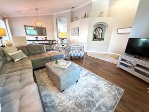 Una sala de estar con sofá modular, reposapiés, sillón y mueble para televisión.