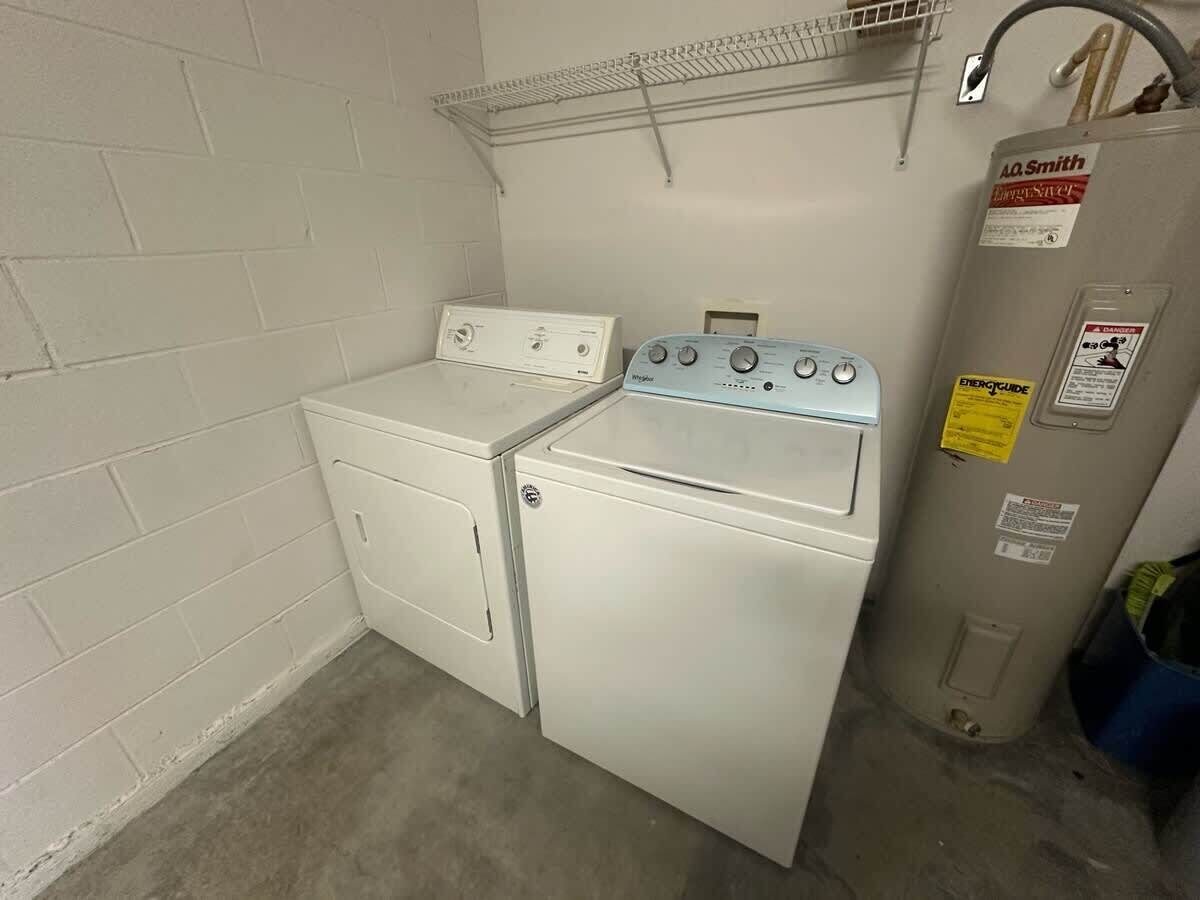A laundry room with a washer and dryer, a metal shelf, and a water heater.