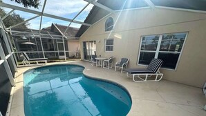 A swimming pool with a curved edge, surrounded by a covered patio area with chairs and a table.