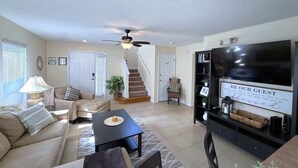 Ein Wohnzimmer mit einer Couch, einem Couchtisch, einem Fernseher und einer Treppe, die in einen anderen Raum führt.