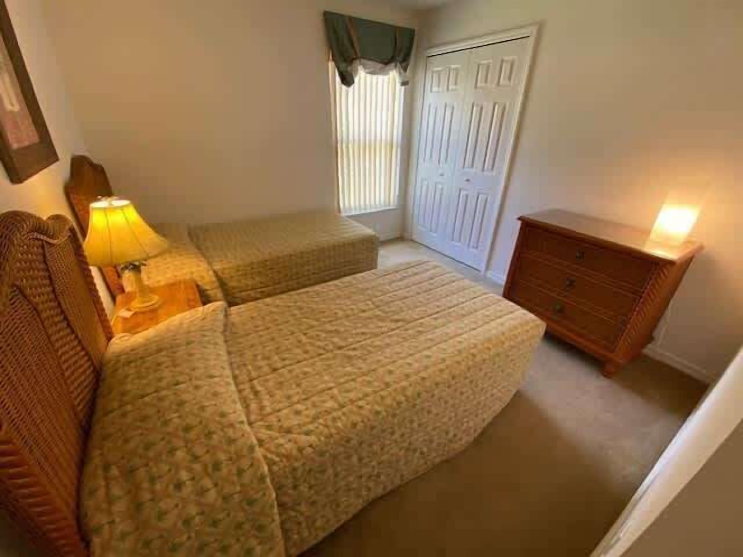 Une chambre avec deux lits, une table de chevet avec une lampe, une commode et une fenêtre avec des rideaux.