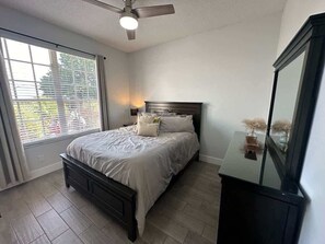 Une chambre à coucher comprenant un lit, un ventilateur de plafond, une table de chevet et une commode.