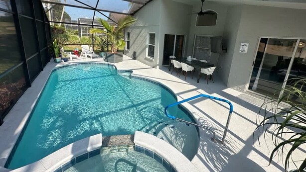 An indoor swimming pool with a glass ceiling, surrounded by lounge chairs and a patio area. - Signature Eight Home (Haines City)