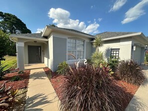Une maison à deux étages avec un porche à l’avant, un garage et un jardin bien entretenu, agrémenté de diverses plantes et arbustes.