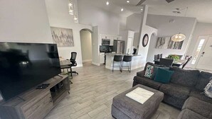 A modern living room with a flat-screen TV, grey sofas, and a wooden entertainment unit. - Signature Eight Home (Haines City)