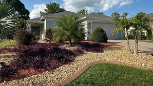 A residential house with a well-maintained lawn, a gravel driveway, and several palm trees. - Signature Eight Home (Haines City)