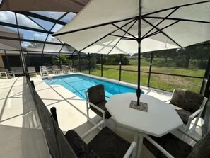 Un área de piscina al aire libre con un porche cubierto, una mesa y sillas.