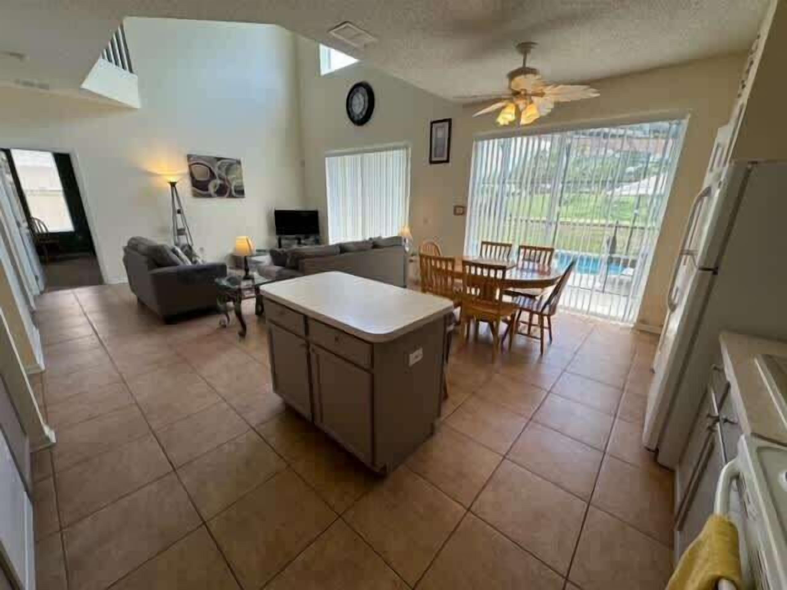 A spacious kitchen with a central island, dining area with chairs, and a living room with a sofa and TV.