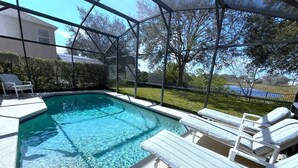 A swimming pool with clear water, surrounded by a covered area with lounge chairs. - Sunset Dunes Villa (Haines City)