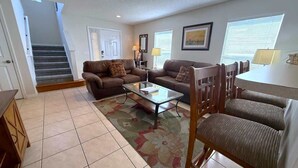 A living room with a sofa set, a coffee table, and a dining area with chairs and a table. - Sunset Dunes Villa (Haines City)