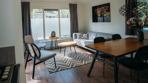 Un salon moderne avec une table à manger en bois, un canapé et une grande fenêtre agrémentée de rideaux.