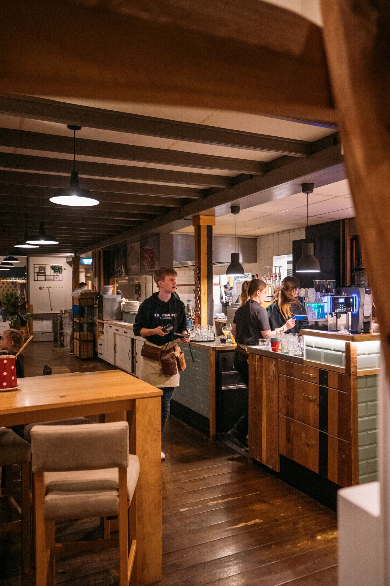 A restaurant interior with wooden floors, a bar area, and a kitchen in the background.