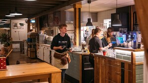 L’intérieur d’un restaurant, avec un sol en bois, un coin bar et une cuisine visible au fond.