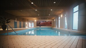 Une piscine intérieure dotée d’un sol carrelé, d’un plafond en bois et de grandes fenêtres.