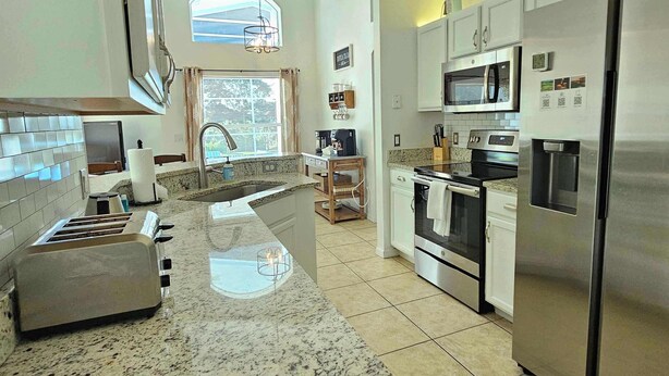 A modern kitchen with granite countertops, stainless steel appliances, and a large window providing natural light. - The Pin Estate (Haines City)