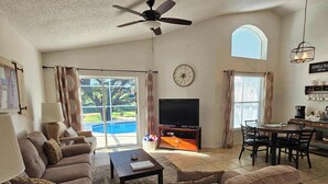 A living room with a sofa, TV, coffee table, and a dining area with chairs and a table. - The Pin Estate (Haines City)