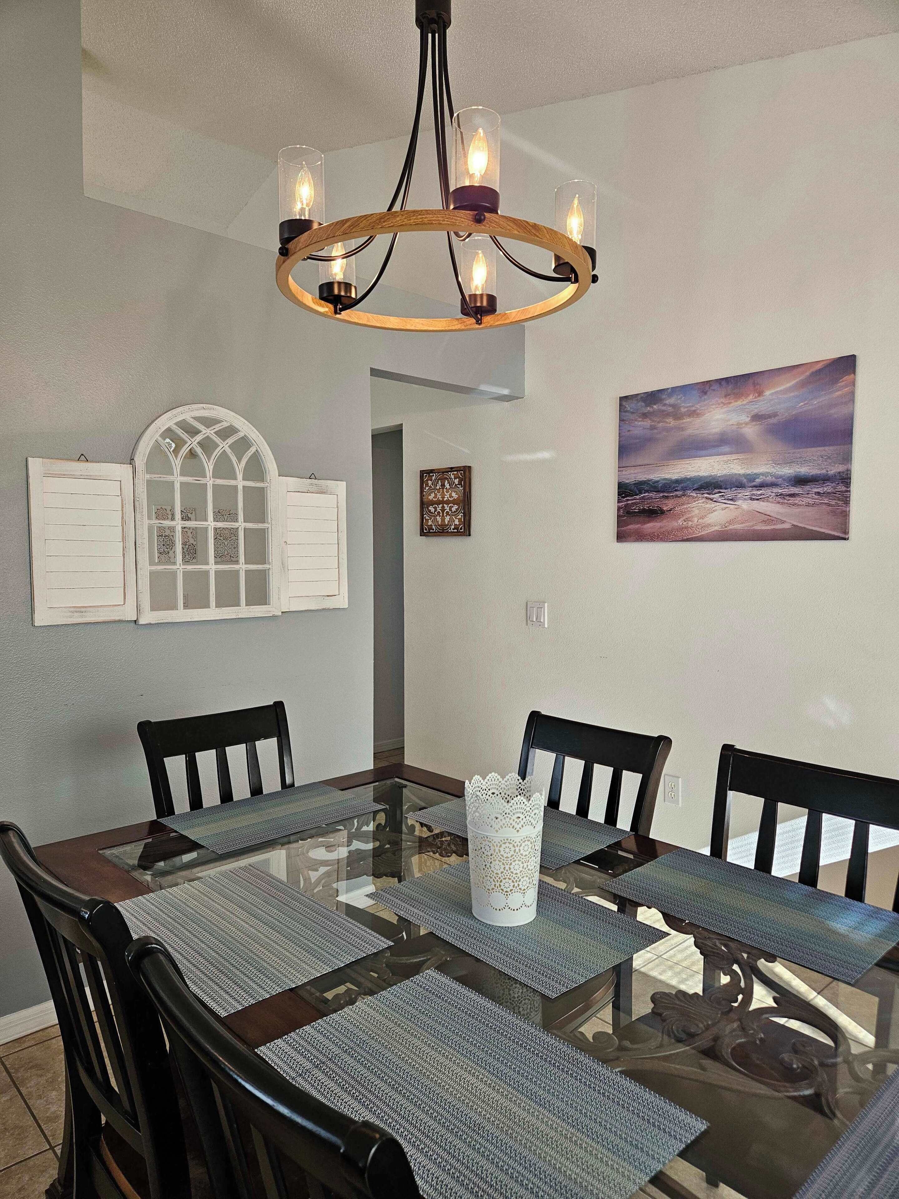 A dining area with a glass-top table, black chairs, and a chandelier.