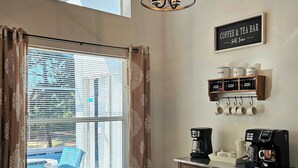 A cozy dining area with a round wooden table, black chairs, a coffee station with two coffee makers, and a sign indicating a coffee and tea bar. - The Pin Estate (Haines City)