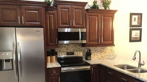 A kitchen with stainless steel appliances, dark wooden cabinets, a granite countertop, and a built-in microwave. - The Palms at Southern Dunes (Haines City)