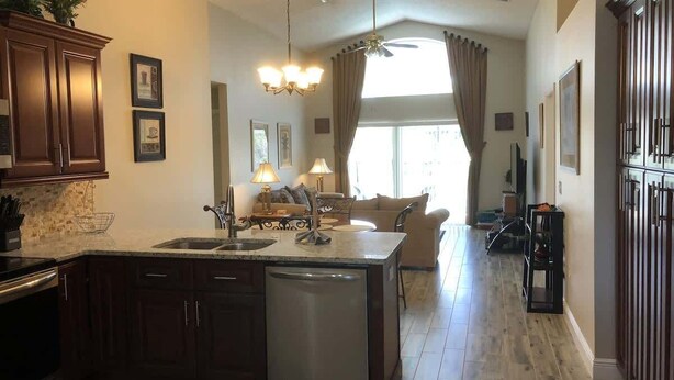 A spacious kitchen with a central island, dark wooden cabinets, and a dishwasher. - The Palms at Southern Dunes (Haines City)
