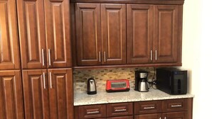 A kitchen with wooden cabinets, a countertop, a toaster, a coffee maker, and a microwave. - The Palms at Southern Dunes (Haines City)