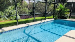 A swimming pool with clear blue water, surrounded by a glass enclosure and a well-maintained garden. - The Palms at Southern Dunes (Haines City)