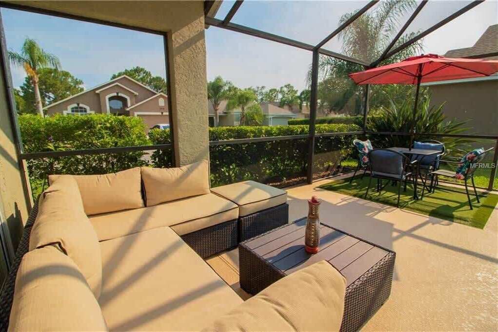A covered outdoor seating area with a sofa and chairs, a table, and a red umbrella.