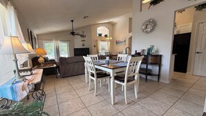 A dining area with a table and chairs, a sofa, a ceiling fan, and a kitchen area with cabinets and a countertop. - Rebecca’s Villa (Haines City)