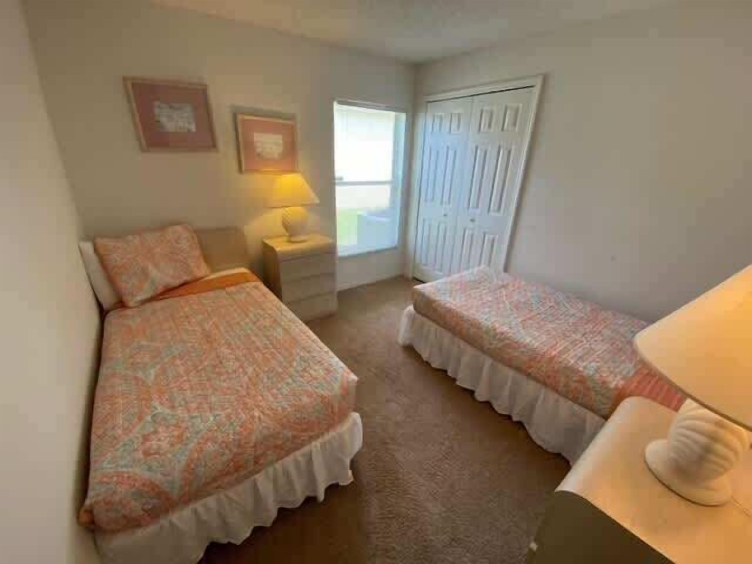 A bedroom with two beds, a nightstand, a lamp, and a door.