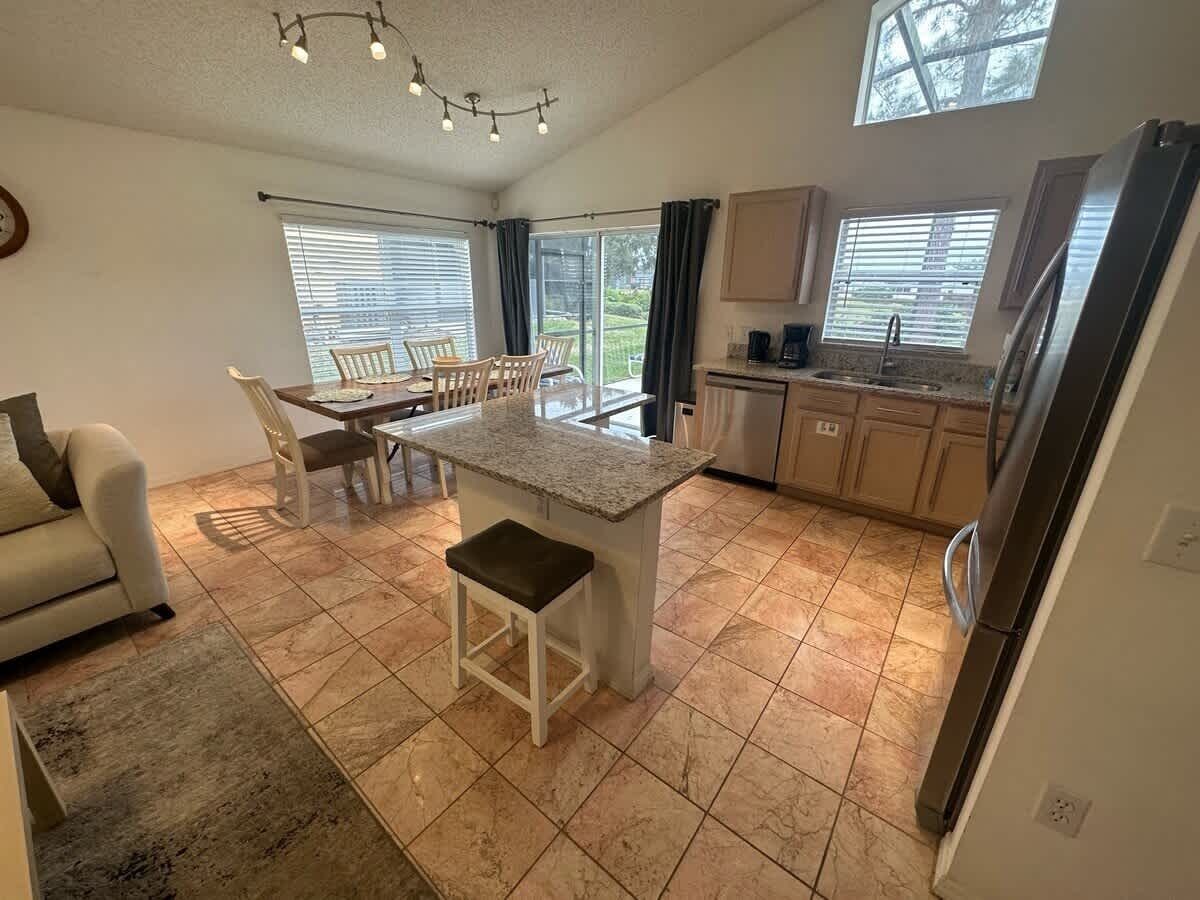 A modern kitchen with a central island, a dining area with chairs, and a sofa.