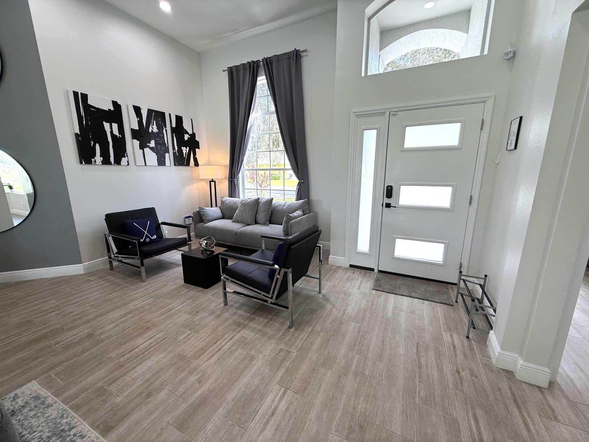 A modern living room with a grey sofa, two armchairs, a coffee table, and a large window with curtains.
