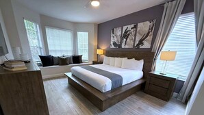 Ein modernes Schlafzimmer mit einem großen Bett, Nachttischen, einem Schreibtisch und einem Fenster mit Jalousien.