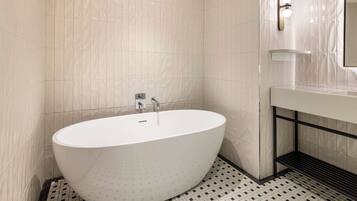 A modern bathroom with a freestanding bathtub, a wall-mounted mirror, and a tiled floor with a geometric pattern.