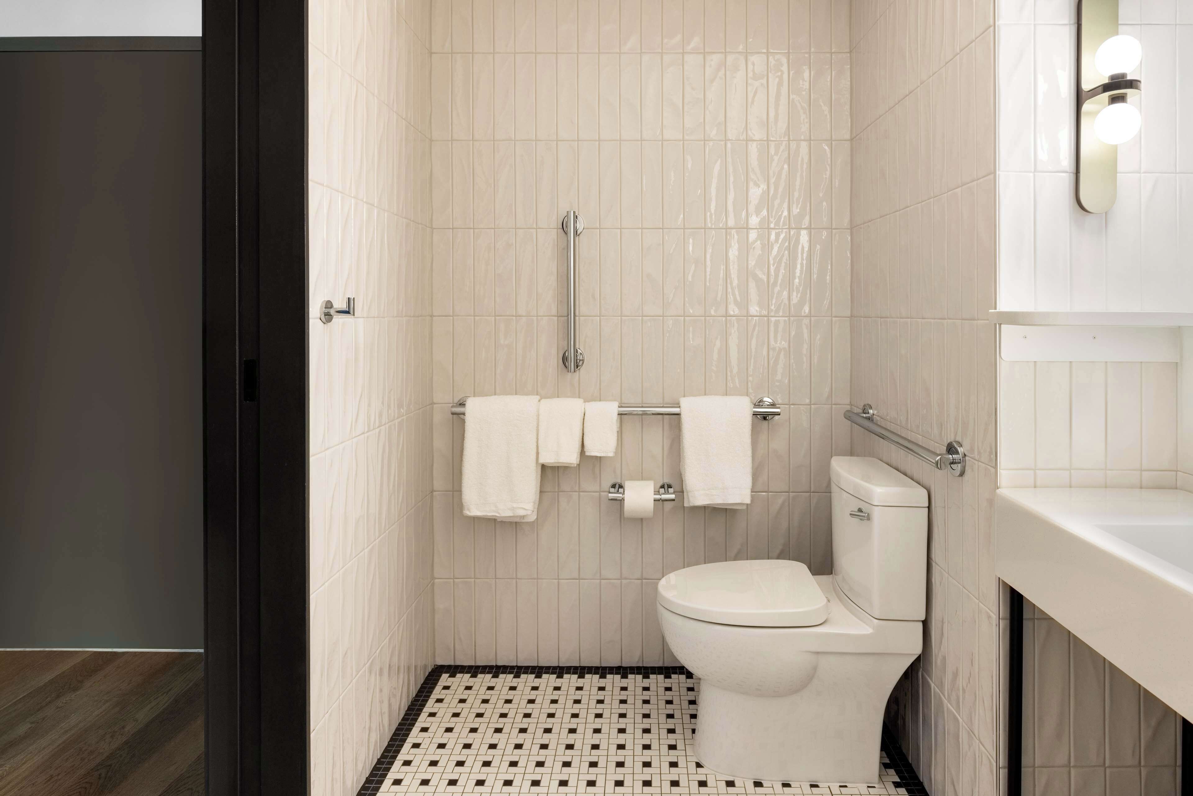 A modern bathroom with a toilet, a handrail, and a towel rack.