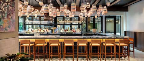 A bar area with multiple hanging light fixtures, a bar counter, and several bar stools.
