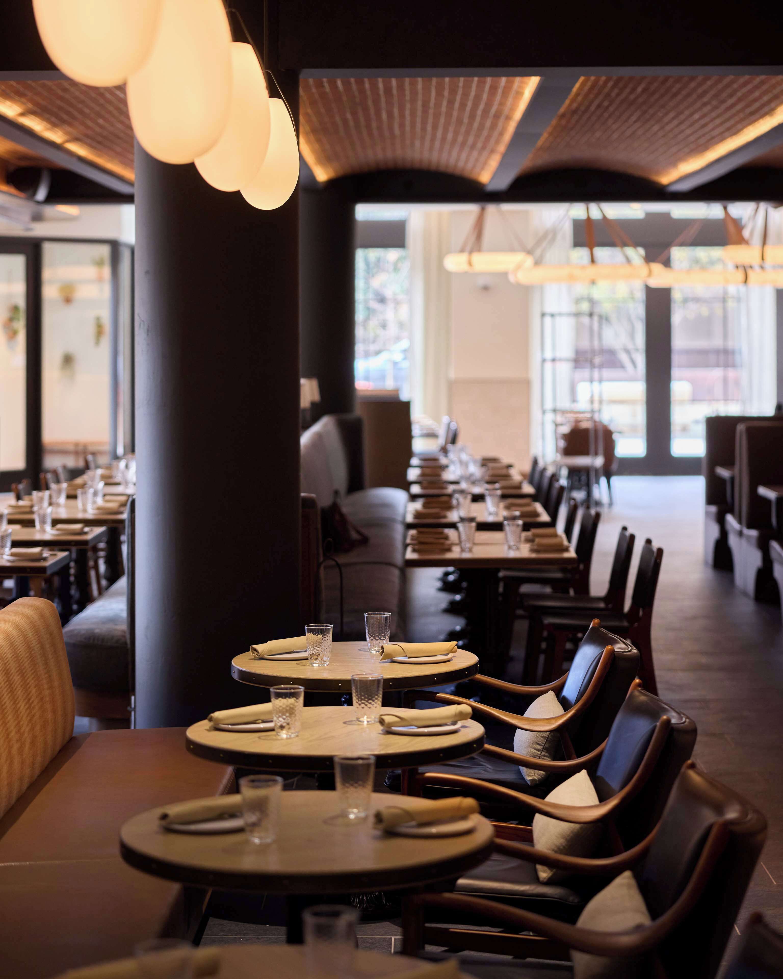 Un restaurante con mesas redondas, sillas e iluminación colgante.