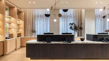 A modern reception area with a central counter, wooden shelving, and a large window with curtains.