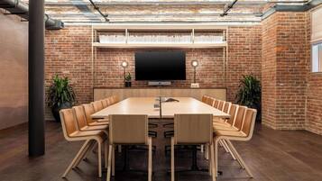 A conference room with a large table, leather chairs, a flat-screen TV, and brick walls.