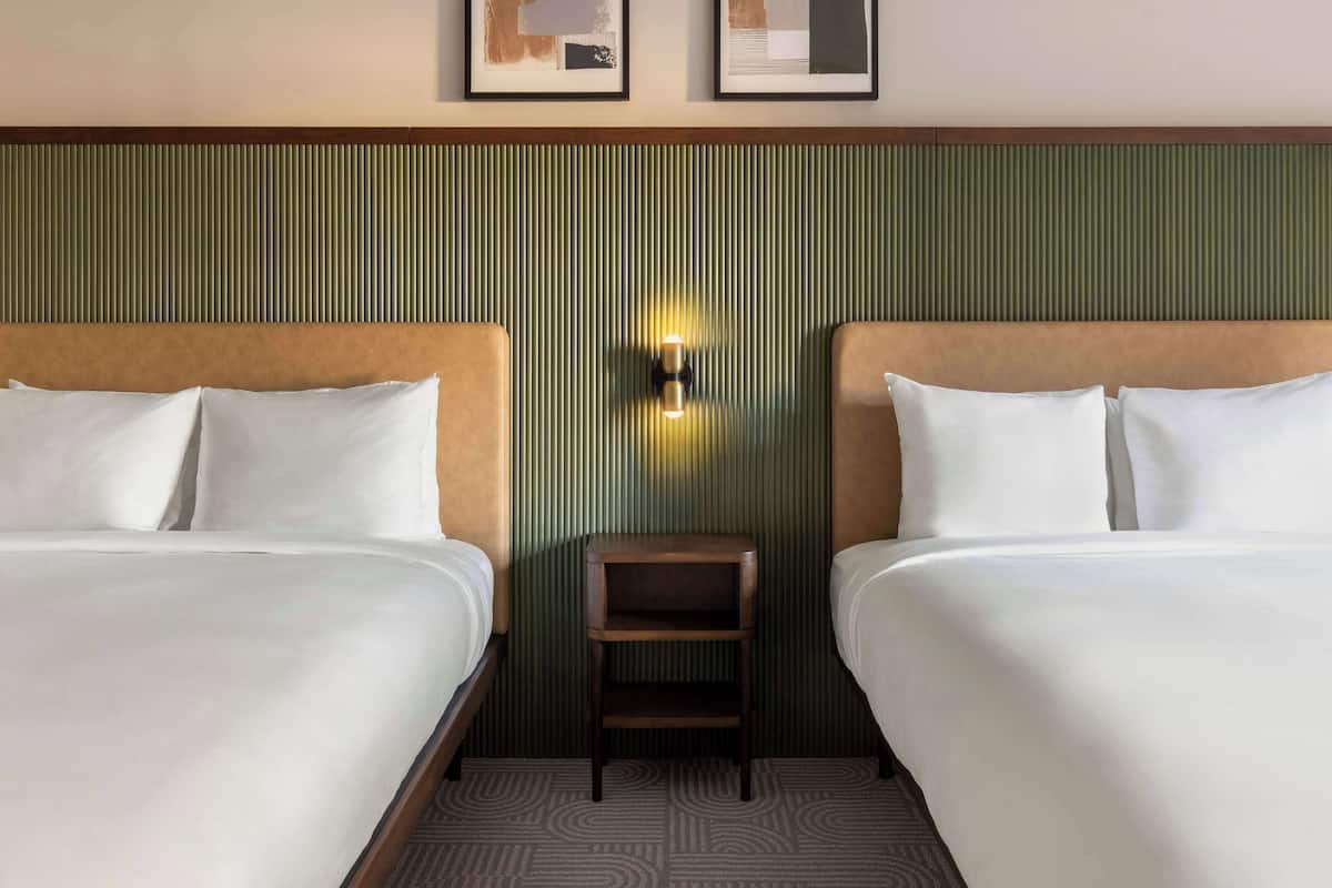Una habitación de hotel con dos camas, una mesita de noche pequeña y una lámpara fijada a la pared.