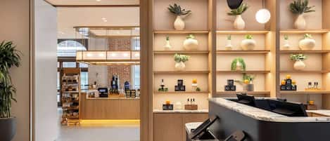 A modern reception area with wooden shelving displaying plants and small items, a marble counter, and a coffee station in the background.
