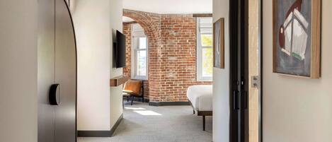 A hallway with a brick wall, a wooden floor, a white door, and a framed picture on the wall.