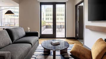 A modern living room with a sofa, a round coffee table, and a chair. There is a sliding glass door leading to an outdoor area with a table and chairs.