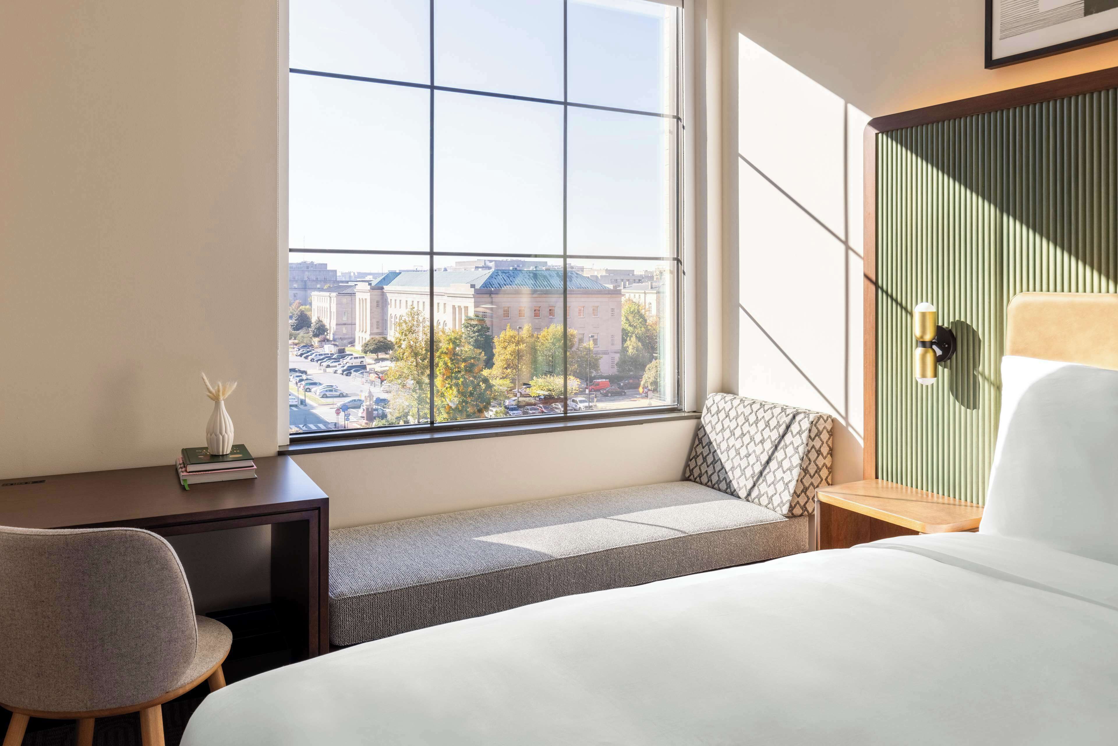 Una habitación de hotel con un ventanal grande, una cama, un escritorio y una silla.