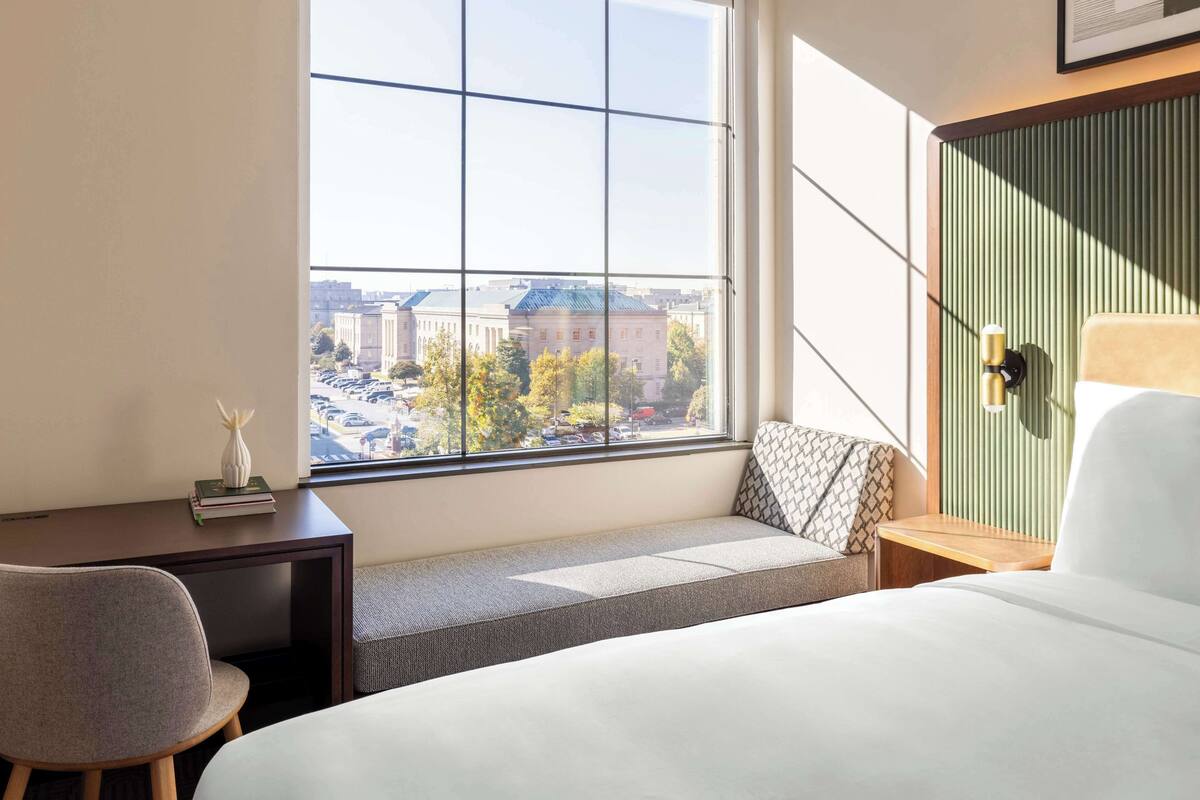 Una habitación de hotel con un ventanal grande, una cama, un escritorio y una silla.