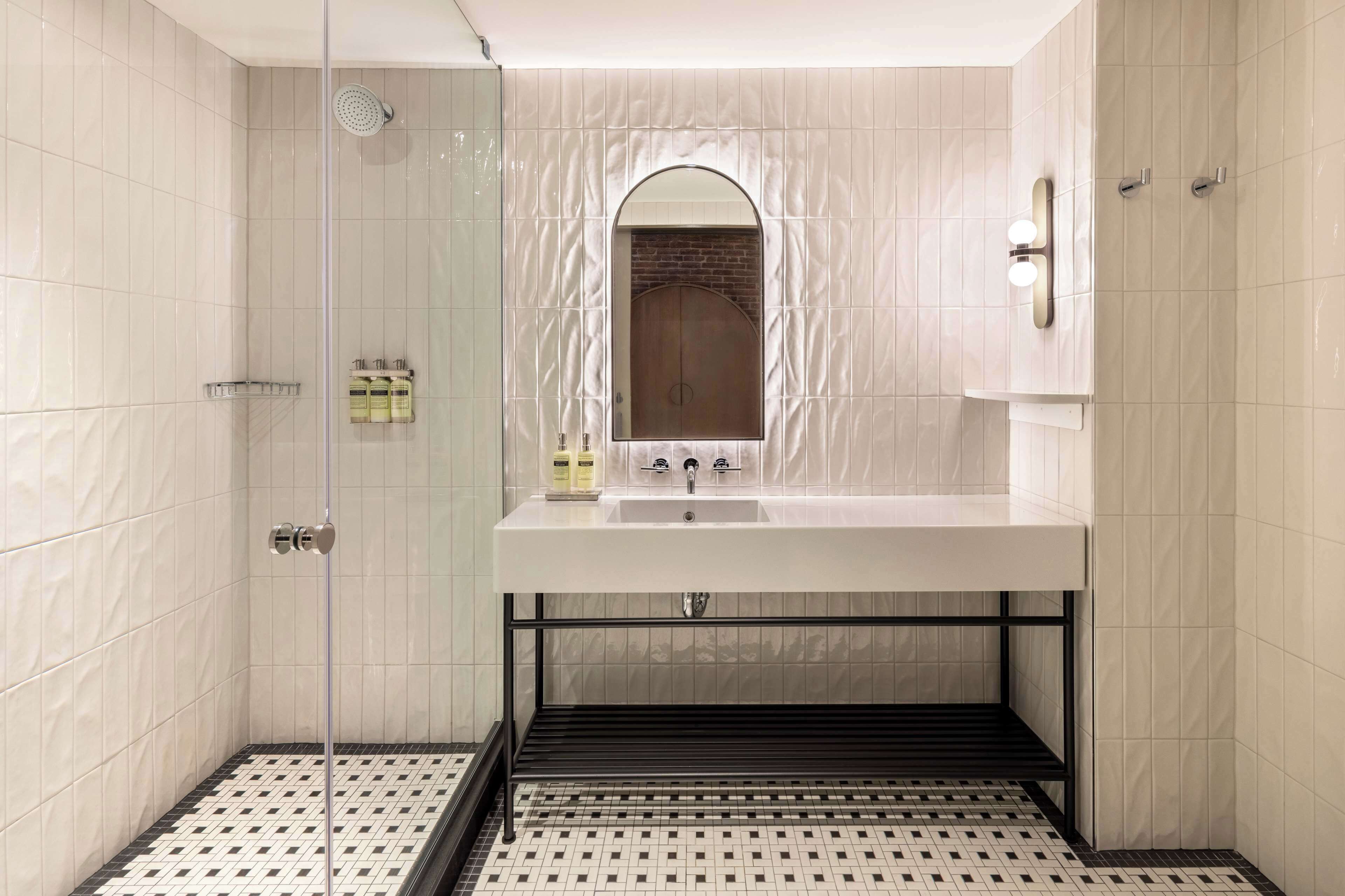 A modern bathroom with a glass-enclosed shower, a white sink with a mirror above, and a patterned floor.