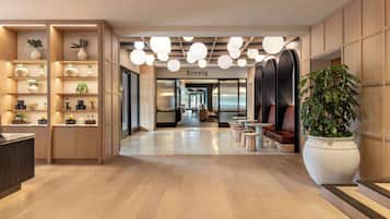 Un moderno vestíbulo de hotel con suelo de madera, un mostrador de recepción y una zona de estar con una planta grande en maceta.