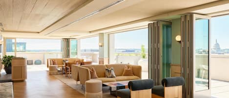 Una sala de estar moderna con un sofá grande, un reposapiés y una mesa de centro, ventanas amplias con vistas a la ciudad y un balcón que ofrece vistas del edificio del Capitolio.