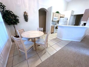 A compact kitchen with a central island, a dining area with a round table and four chairs, and a potted plant. - Liquid Sunshine Villa (Haines City)